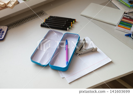 Desk with empty pencil case, pens, notebook, and stapler in study setting 141603699
