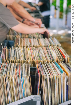 Shoppers browse rows of used vinyl records displayed in boxes at outdoor market, vintage music, nostalgia mood, retro grainy texture 141604121