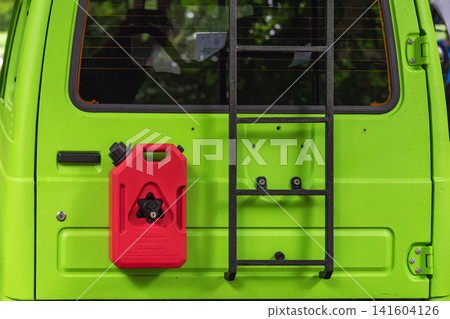 Rear of bright green customized off-road vehicle shows an externally mounted red gasoline can and black metal ladder at automobile event 141604126