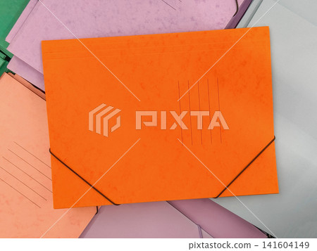 Bright orange cardboard document folder with elastic closure surrounded by pastel office folders. Colorful stationery composition for filing, organization, education and back to school designs 141604149