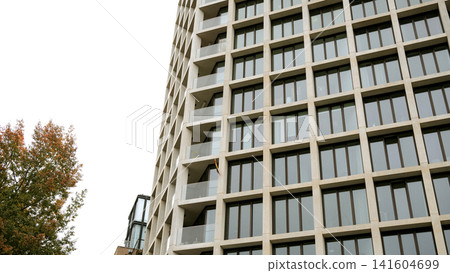 Modern high-rise apartment building with geometric facade and autumn tree Modern high-rise apartment building with geometric facade and autumn tree 141604699