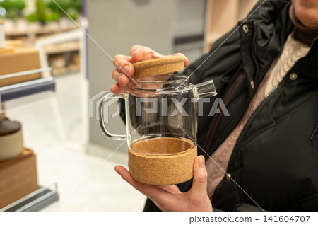 Female hands holding cork-base glass teapot in store Female hands holding cork-base glass teapot in store 141604707
