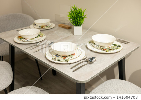 Elegant dining table setup with white dishware and green plant decor Elegant dining table setup with white dishware and green plant decor 141604708