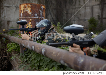 A soldier aims a gun while leaning on a pipe, lying on the ground A soldier aims a gun while leaning on a pipe, lying on the ground 141605299
