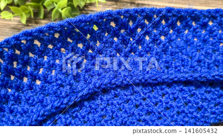 A blue thread pattern on a wooden background. Knitting tutorial and sample of the finished piece. A blue thread pattern on a wooden background. Knitting tutorial and sample of the finished piece. 141605432