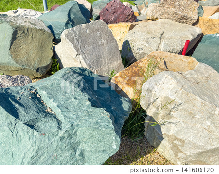 Varied natural stones and rocks in outdoor setting with grass and sunlight illuminating surface Varied natural stones and rocks in outdoor setting with grass and sunlight illuminating surface 141606120