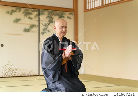一幅僧侶坐在日式房間裡的肖像,他手持折扇和念珠。 一幅僧侶坐在日式房間裡的肖像,他手持折扇和念珠。 141607251