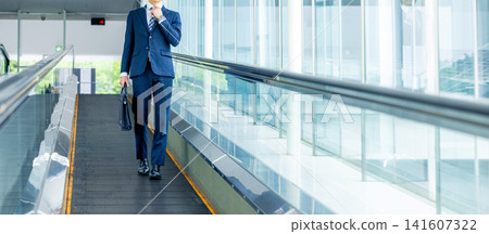 Businessman riding escalator Businessman riding escalator 141607322