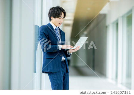 一位年輕的商人正在辦公室走廊使用筆記型電腦。 一位年輕的商人正在辦公室走廊使用筆記型電腦。 141607351