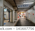 Graffiti on the right wall; a shopping street continues straight ahead; the old, worn floor of the passageway in front of the ticket gate. 141607756