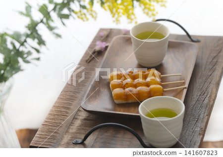御手洗團子和綠茶擺放在木托盤上,沐浴在春日的陽光下。 御手洗團子和綠茶擺放在木托盤上,沐浴在春日的陽光下。 141607823