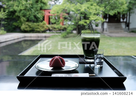 Enjoying Japanese sweets and cold tea while gazing at the fresh greenery of a beautiful Japanese garden. Enjoying Japanese sweets and cold tea while gazing at the fresh greenery of a beautiful Japanese garden. 141608214