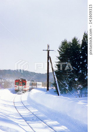 A JR Hanawa Line Kiha 52 train travels through a snow-covered winter landscape (Appi Kogen Station, heavy snowfall, vertical composition). A JR Hanawa Line Kiha 52 train travels through a snow-covered winter landscape (Appi Kogen Station, heavy snowfall, vertical composition). 141609315