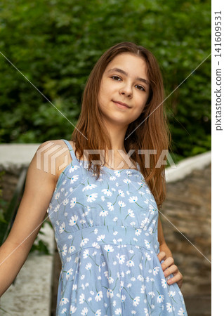 Portrait of a girl in a blue floral summer dress smiling outdoors on stone steps Portrait of a girl in a blue floral summer dress smiling outdoors on stone steps 141609531