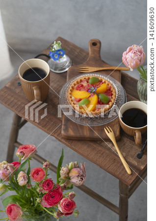 木桌上擺放著水果塔和兩杯熱咖啡。鮮花環繞,是享受咖啡館時光的好去處。 木桌上擺放著水果塔和兩杯熱咖啡。鮮花環繞,是享受咖啡館時光的好去處。 141609630