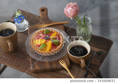 木桌上擺放著水果塔和兩杯熱咖啡。鮮花環繞,是享受咖啡館時光的好去處。 木桌上擺放著水果塔和兩杯熱咖啡。鮮花環繞,是享受咖啡館時光的好去處。 141609631