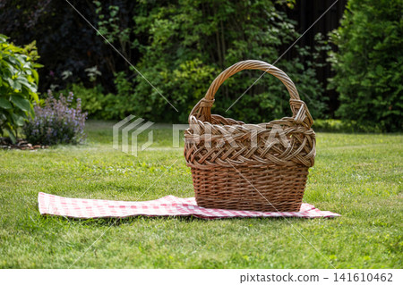 Empty wicker picnic basket on blanket in green garden with copy space Empty wicker picnic basket on blanket in green garden with copy space 141610462