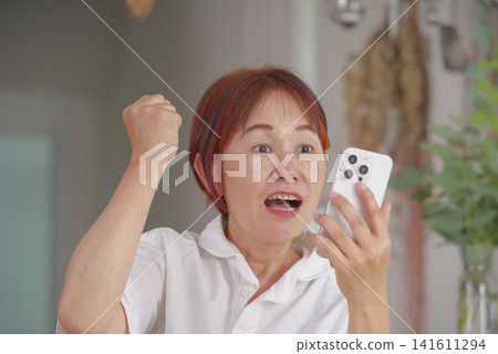中年婦女一邊看著智慧型手機一邊做出得意的手勢。 141611294