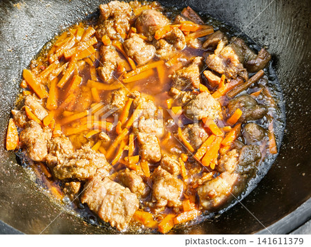 A kazan sits over a fire as meat and carrots cook together to make pilaf. This is a traditional dish prepared outdoors, often enjoyed in gatherings A kazan sits over a fire as meat and carrots cook together to make pilaf. This is a traditional dish prepared outdoors, often enjoyed in gatherings 141611379