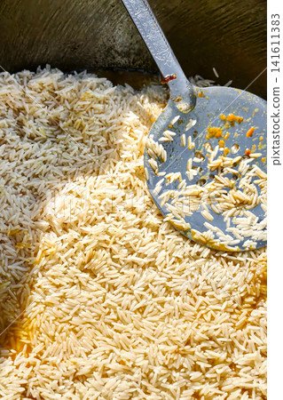 Rice is being prepared in a kazan as part of making pilaf. Spices and ingredients are mixed in the pot to create a flavorful dish Rice is being prepared in a kazan as part of making pilaf. Spices and ingredients are mixed in the pot to create a flavorful dish 141611383