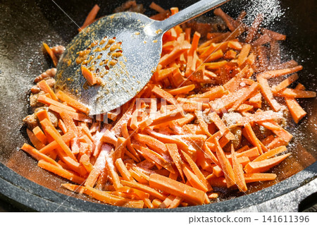 Sliced carrots are being cooked in a kazan with spices added. The preparation is for pilaf, a dish typical in many cultures Sliced carrots are being cooked in a kazan with spices added. The preparation is for pilaf, a dish typical in many cultures 141611396