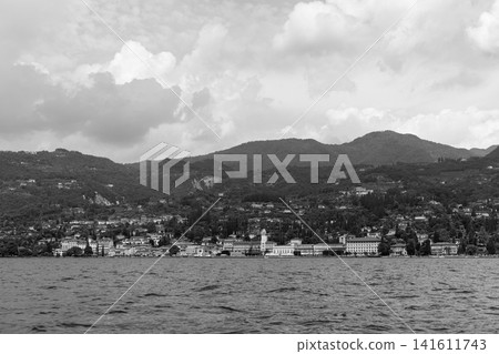 Vintage monochrome travel view of Gardone Riviera on Lake Garda from the water, layered hillside villas and cypress trees rise beneath dramatic clouds above the rippled lakefront for nostalgic Italian Vintage monochrome travel view of Gardone Riviera on Lake Garda from the water, layered hillside villas and cypress trees rise beneath dramatic clouds above the rippled lakefront for nostalgic Italian 141611743