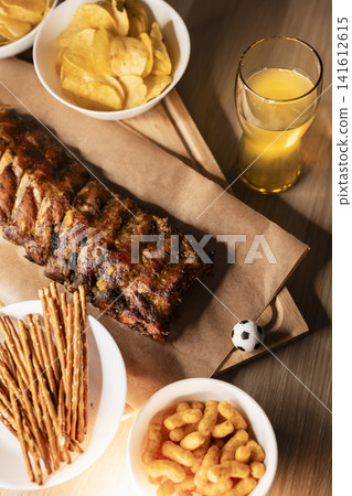Barbecue ribs on a wooden board, beer and snacks arranged for a soccer viewing party, creating a cozy sport night atmosphere. Barbecue ribs on a wooden board, beer and snacks arranged for a soccer viewing party, creating a cozy sport night atmosphere. 141612615