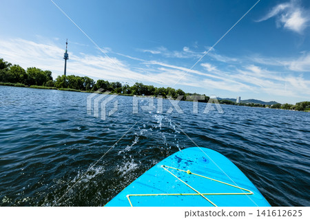 Turquoise paddleboard in the middle of a calm river with a water splash in the foreground, illustrating summer water sport. Turquoise paddleboard in the middle of a calm river with a water splash in the foreground, illustrating summer water sport. 141612625
