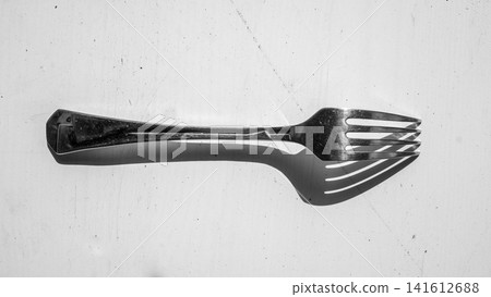 Metal fork resting on rough concrete surface with dramatic side lighting, strong shadow, monochrome kitchen utensil still life and minimal background for dining concept Metal fork resting on rough concrete surface with dramatic side lighting, strong shadow, monochrome kitchen utensil still life and minimal background for dining concept 141612688