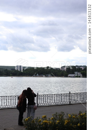 Two girls take photos of a lake at sunset. Two girls take photos of a lake at sunset. 141613132