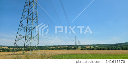 High-voltage electricity pylon over a rural field under clear blue sky with copy space. Concept of power grid, energy infrastructure and industry. High-voltage electricity pylon over a rural field under clear blue sky with copy space. Concept of power grid, energy infrastructure and industry. 141613370
