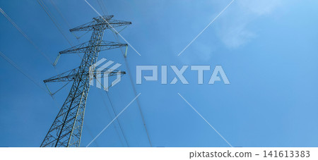 Low angle view of a high-voltage electricity pylon against clear blue sky with copy space. Concept of power grid, energy supply and infrastructure Low angle view of a high-voltage electricity pylon against clear blue sky with copy space. Concept of power grid, energy supply and infrastructure 141613383