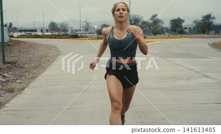 Woman running toward camera on an open road Woman running toward camera on an open road 141613485