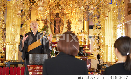 一位佛教僧侶在寺廟內殿佈道,周圍是身著喪服的哀悼者。 一位佛教僧侶在寺廟內殿佈道,周圍是身著喪服的哀悼者。 141613627