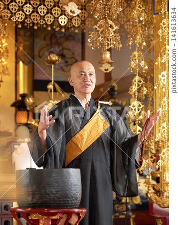 A monk giving a sermon in the main hall of a temple, holding prayer beads. A monk giving a sermon in the main hall of a temple, holding prayer beads. 141613634