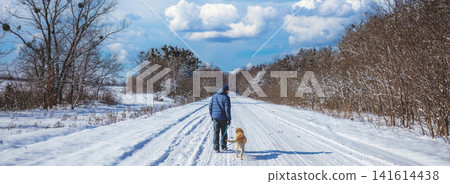 Man with the dog on a leash walks in a snowy road in winter Man with the dog on a leash walks in a snowy road in winter 141614438