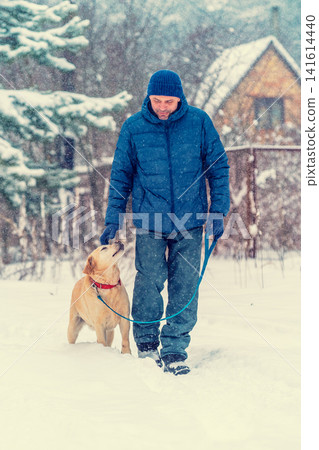 Man and dog are best friends. A man with a dog walks in a village in a snowy winter Man and dog are best friends. A man with a dog walks in a village in a snowy winter 141614440