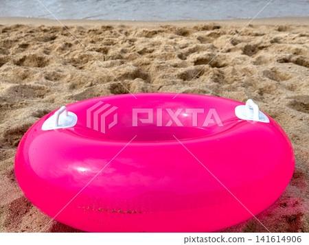 Bright pink inflatable swim ring on sandy beach. Bright pink inflatable swim ring on sandy beach. 141614906