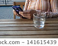 A woman with a mobile phone and a glass of water 141615439