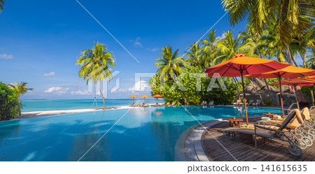 Idyllic tropical infinity pool with red umbrellas and loungers beside turquoise ocean palm trees blue sky. Perfect summer vacation travel resort paradise. Luxury getaway relax scenic 141615635