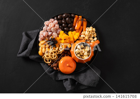 Halloween snack platter with pumpkin mug and spooky treats on black background top view Halloween snack platter with pumpkin mug and spooky treats on black background top view 141615708