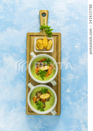 Creamy cauliflower soup with toasted bread croutons on blue tabletop. Vegetarian healthy food concept. Ideas and recipes for winter meal. Top view, flat lay. Creamy cauliflower soup with toasted bread croutons on blue tabletop. Vegetarian healthy food concept. Ideas and recipes for winter meal. Top view, flat lay. 141615786