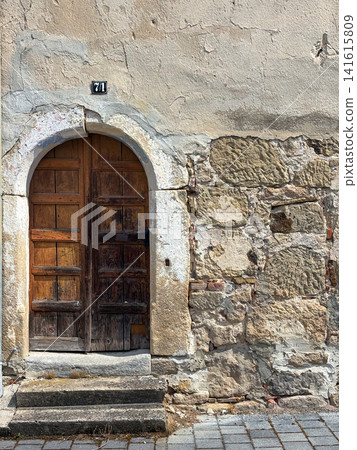 Weathered arched wooden door with house number 71 on aged stone wall in Steinenbronn, Germany 141615809