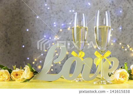 Two Champagne glasses with yellow bows standing on table with love letters and roses, bokeh lights, St. Valentine or wedding greeting card Two Champagne glasses with yellow bows standing on table with love letters and roses, bokeh lights, St. Valentine or wedding greeting card 141615838