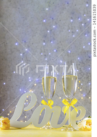 Two Champagne glasses with yellow bows standing on table with love letters and roses, bokeh lights, St. Valentine or wedding greeting card Two Champagne glasses with yellow bows standing on table with love letters and roses, bokeh lights, St. Valentine or wedding greeting card 141615839