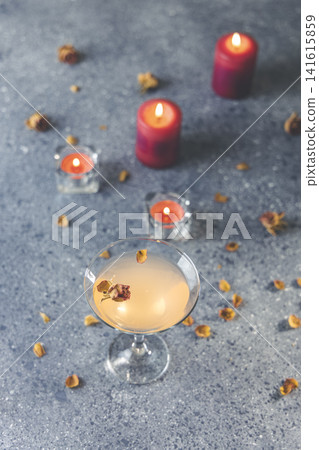Overhead view of grapefruit martini cocktail with dried roses flowers and petals, surrounded candles on dark gray table surface. Overhead view of grapefruit martini cocktail with dried roses flowers and petals, surrounded candles on dark gray table surface. 141615859