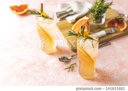 Two glasses of Paloma cocktails with tequila fresh grapefruit juice combined and rosemary. Light pink concrete surface. Two glasses of Paloma cocktails with tequila fresh grapefruit juice combined and rosemary. Light pink concrete surface. 141615881