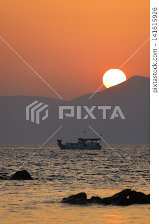 a lonely fishing boat in the sea as the sun sets behind the mountains a lonely fishing boat in the sea as the sun sets behind the mountains 141615926