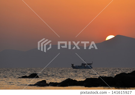 a lonely fishing boat in the sea as the sun sets behind the mountains a lonely fishing boat in the sea as the sun sets behind the mountains 141615927