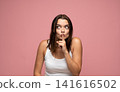 Woman making a shush gesture with finger on lips, asking for silence and mystery on a pink studio background 141616502